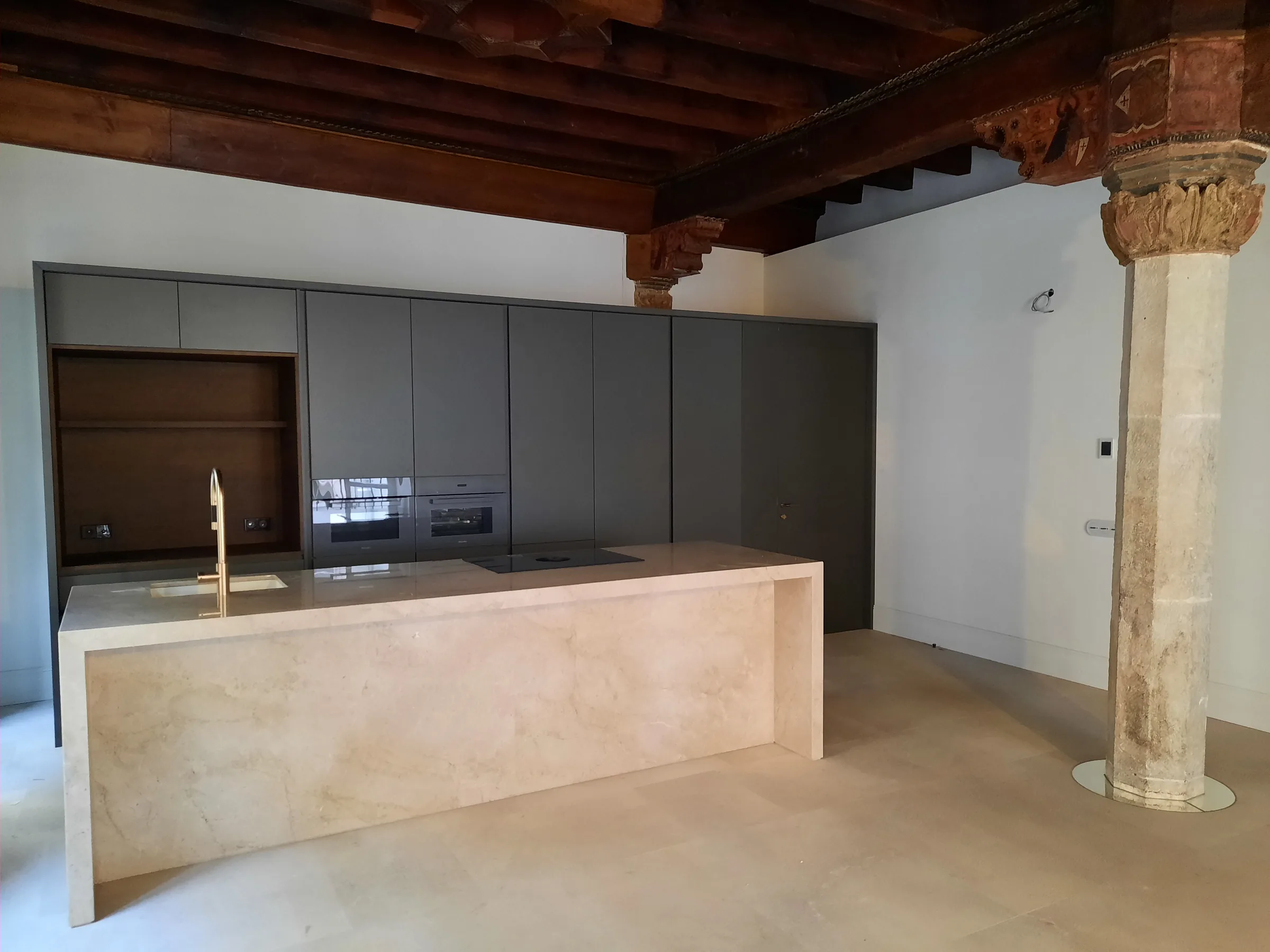 Kitchen inside a renovated historic building in central Palma, with an original stone column and wooden beams.